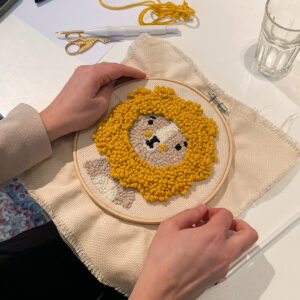 Dicht gestickter Punch-Needle-Löwe im Stickrahmen, Nahaufnahme der gelben und beigen Garnschlaufen.