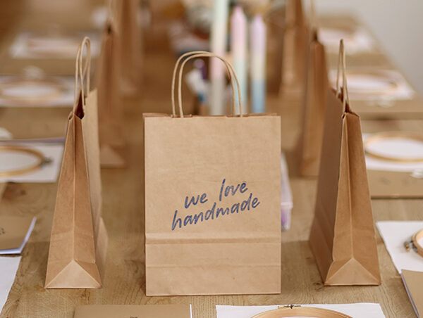 Kreativ-Workshop Set-Up von we love handmade in Wien: Holztisch mit Stickrahmen, Workbooks und Papiertüten mit Logo für DIY-Teilnehmer:innen.