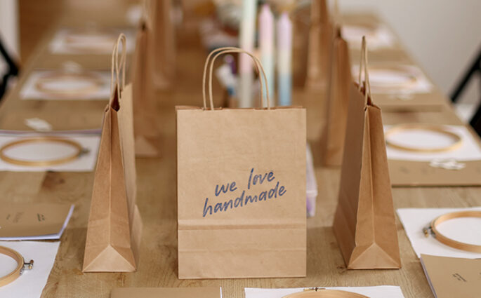 Kreativ-Workshop Set-Up von we love handmade in Wien: Holztisch mit Stickrahmen, Workbooks und Papiertüten mit Logo für DIY-Teilnehmer:innen.