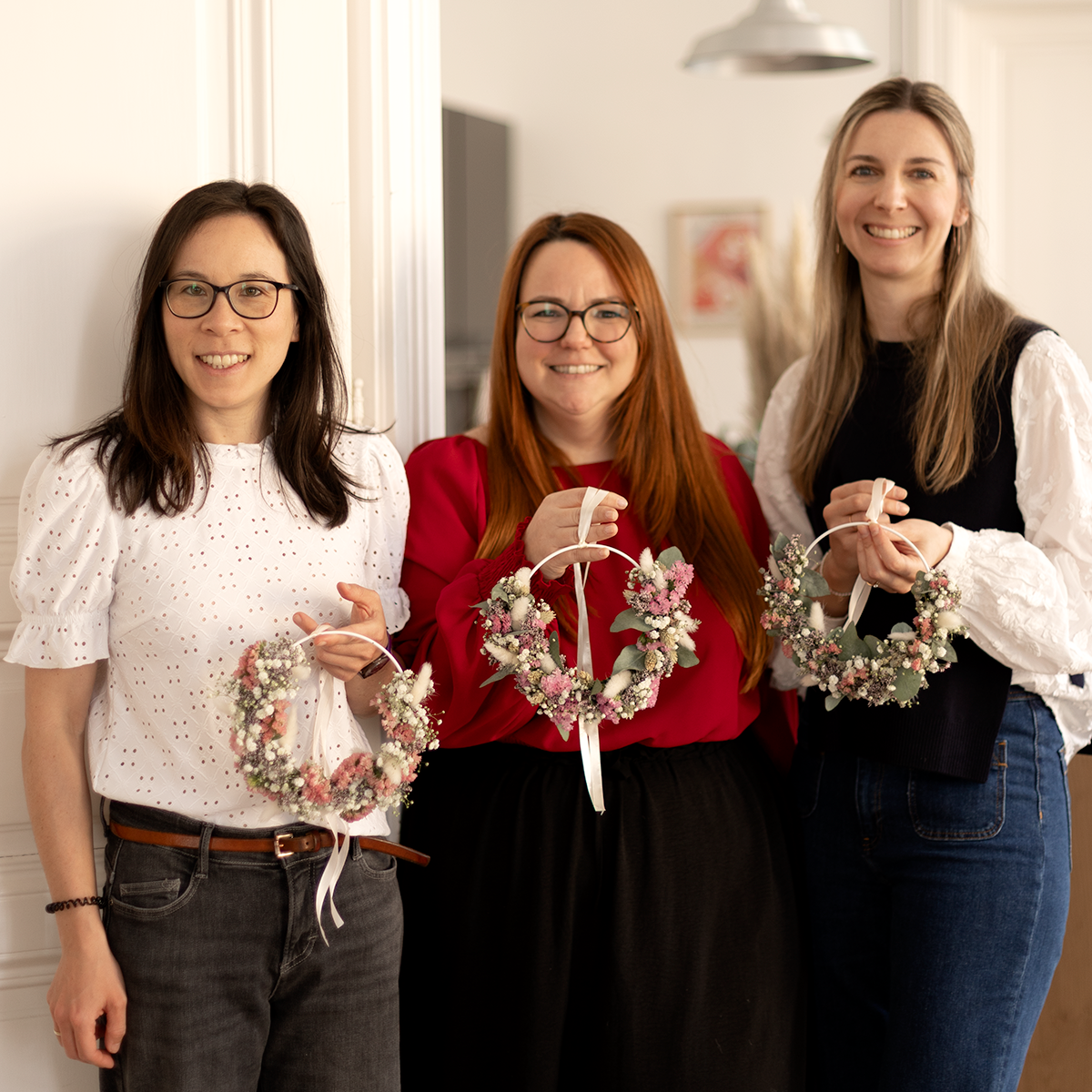 Drei glückliche Teilnehmerinnen präsentieren ihre selbst gebundenen Flowerhoops in rosa-weißen Farbtönen im hellen we love handmade Workshop-Studio in Wien Neubau.