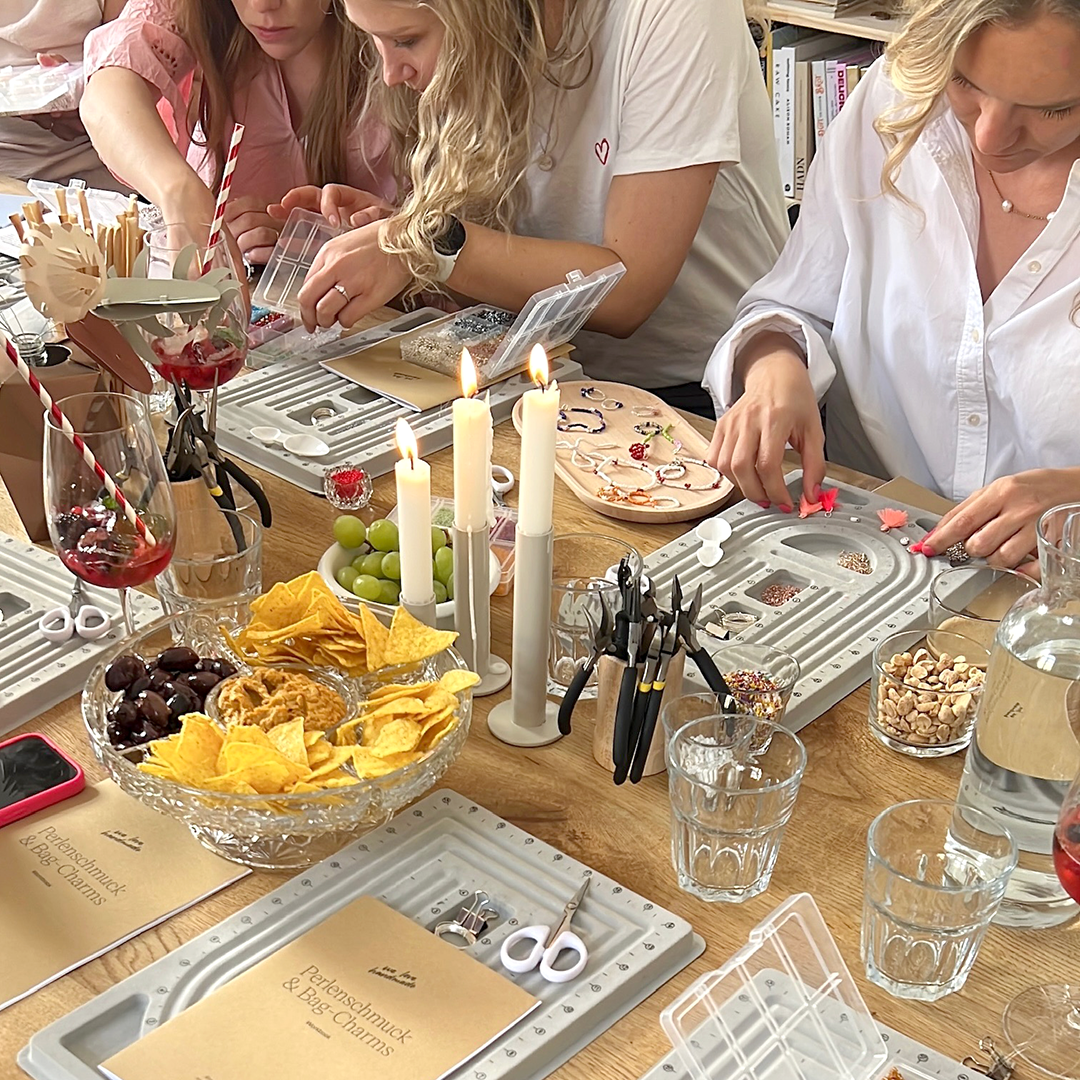 Teilnehmerinnen beim Perlenschmuck Workshop in Wien Neubau an einem reich gedeckten Tisch mit Perlen-Buffet, Snacks und Kerzenschein. | we love handmade