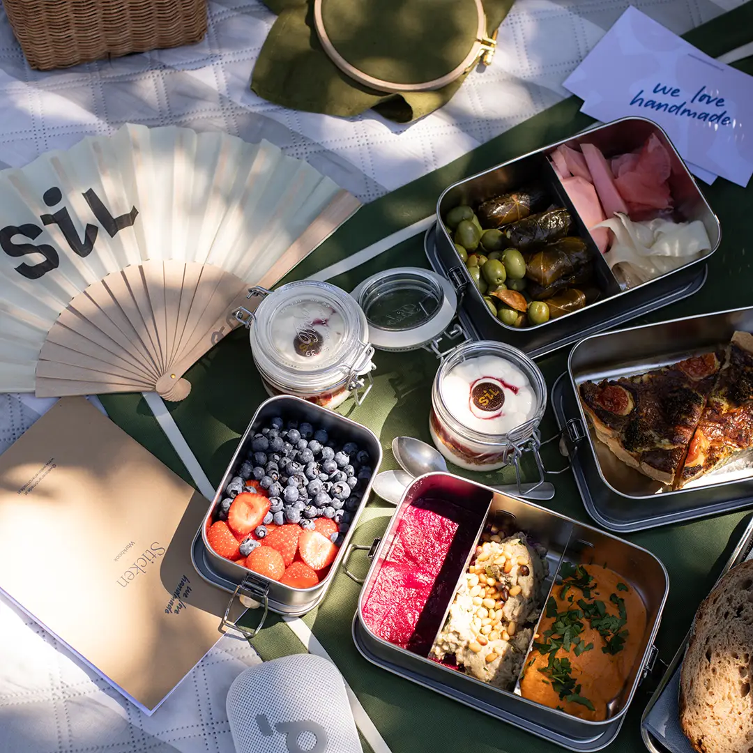 SiL Picknickkorb Inhalt mit Oliven, Weinblättern, Joghurt und Quiche neben Stickutensilien