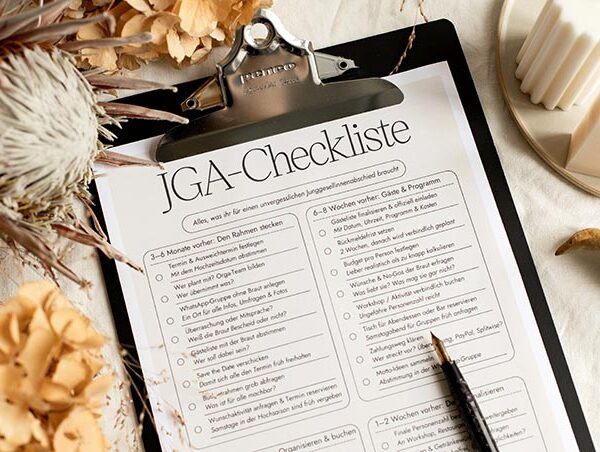 Nahaufnahme im Querformat von der ausgedruckten JGA-Checkliste im Klemmbrett, umrahmt von Trockenblumen und Kerzen.